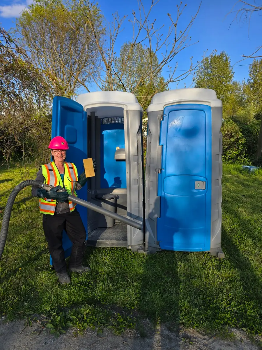 Clearset Vac Truck Services Portable Toilet Rental Services Clearset VAC Truck employee wearing PPE and holding septic pumping equipment outside of one of their portable toilet rentals in Vancouver.