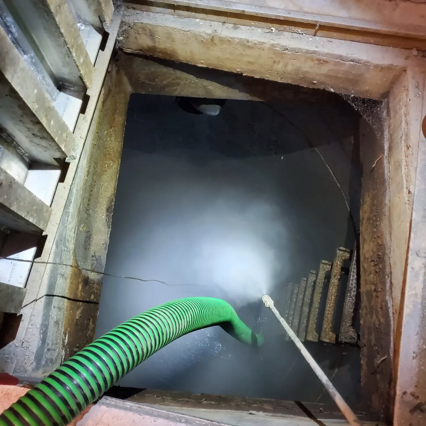 Close-up of an open underground parkade pump chamber with a sediment removal hose from Clearset