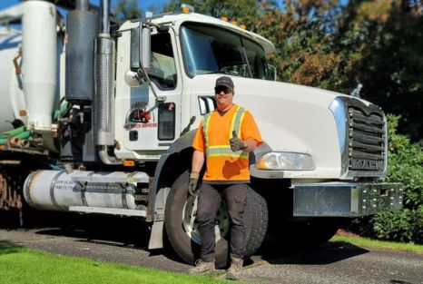 Friendly looking Clearset VAC Truck employee, wearing high-vis PPE, standing in front of their branded vacuum truck, giving a thumbs-up.