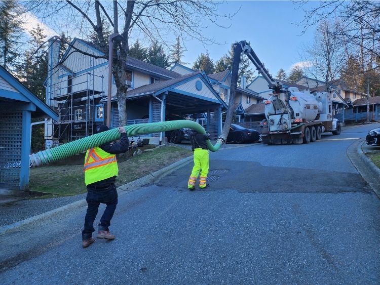 Two Clearset employees, wearing bright PPE, carrying the tube from the vacuum truck to perform a hydrovac excavation in Vancouver