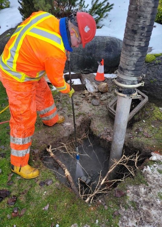 Clearset Vac Truck Services employee, in bright orange PPE, performing a potholing service in BC